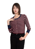 A woman modeling a cropped, long-sleeve knit cardigan with horizontal burgundy and white stripes, navy blue ribbed collar, cuffs, and hem, paired with black pants against a solid gray studio background.