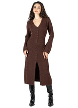 A woman modeling a long brown knit cardigan dress with a V-neck, front buttons, and long sleeves, paired with black knee-high boots, against a light gray studio background.
