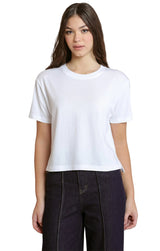 A woman modeling a plain white short-sleeve crewneck crop top paired with dark charcoal pants, set against a solid light gray studio background.