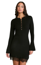 A woman modeling a black ribbed long-sleeve mini dress with a buttoned henley-style neckline and black lace hem, photographed against a plain light gray studio background.