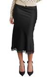 A black satin midi skirt with a sheer lace hem, styled with a cream polka-dot cardigan and black pointed-toe heels against a light gray studio background.