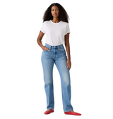 A woman modeling light-wash blue straight-leg jeans with a white t-shirt and red flats, standing against a plain light gray studio background.