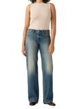 A model wearing a pair of medium-wash blue jeans with a faded light wash on the thighs and knees, paired with a beige sleeveless top and dark brown shoes, against a light gray studio background.