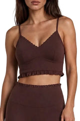 A woman wearing a dark brown ruffled crop top and matching high-waisted bottoms against a light gray studio background.