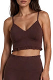 A woman wearing a dark brown ruffled crop top and matching high-waisted bottoms against a light gray studio background.