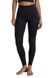 Black high-waisted leggings with a small repeating geometric pattern, modeled on a person standing barefoot against a light gray concrete wall and floor.