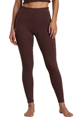 A model wearing high-waisted, dark brown leggings, shown from the waist down against a neutral light gray studio background.