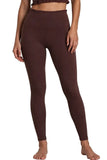 A model wearing high-waisted, dark brown leggings, shown from the waist down against a neutral light gray studio background.